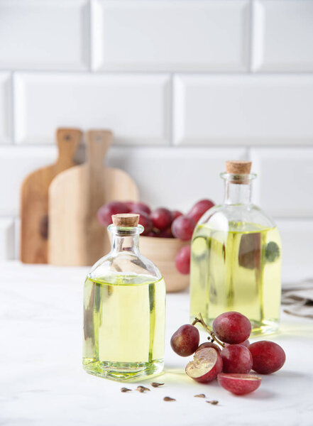 натуральное диетическое и веганское масло виноградных косточек в стеклянных бутылках на белом мраморном фоне. Здоровое питание и образ жизни. Вид спереди 