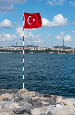 Kızıl Türk bayrağı güneşli bir yaz gününde Boğaz 'ın taştan kıyısında duruyor. Koronavirüs salgını nedeniyle ülkede tecrit. İstanbul, Türkiye