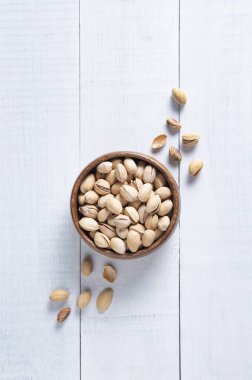 Beyaz ahşap arka planda kahverengi bir kasede fıstıklı fıstık. Üst görünüm ve boşluk resmi kopyala