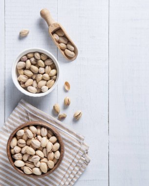 Fıstıklı fıstıklar kaselerde, kesme tahtasının üzerinde ve beyaz ahşap arka planda bir kaşıkta yatıyordu. Üst görünüm ve boşluk resmi kopyala