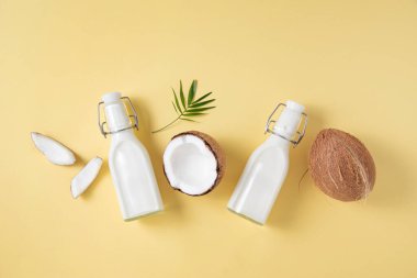 Sağlıklı düz konsept. Vejetaryen süt şişeleri, hindistan cevizi dilimleri ve sarı arka planda palmiye dalı. Üst görünüm ve boşluk resmi kopyala