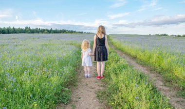 İki kız güneşli bir yaz gününde güzel bir çiçek tarlasında yürür.