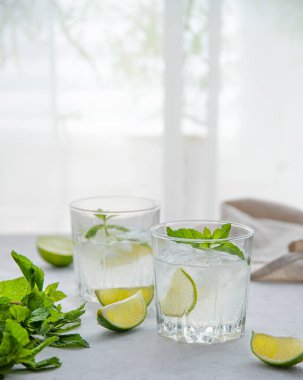 Masada iki bardak limonata mojito ve limon dilimleri ve pencerenin sabah ışığında nane şekeri. Ön görünüm resmi