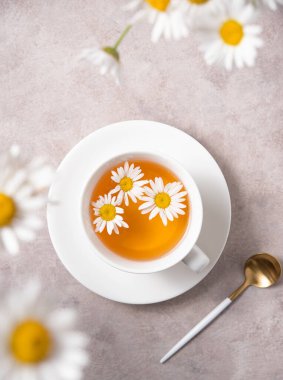 Beyaz bir fincanda papatya çayı ve pembe-gri arka planda papatya çiçeği. Üst görünüm ve resmi kapat