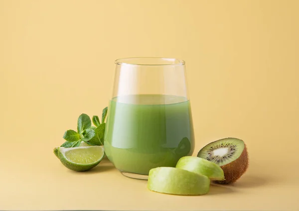 Smoothie made of green kiwi fruits, apple, lime and mint in a glass on a yellow background. The concept of a healthy detox drink. Front view and copy space image