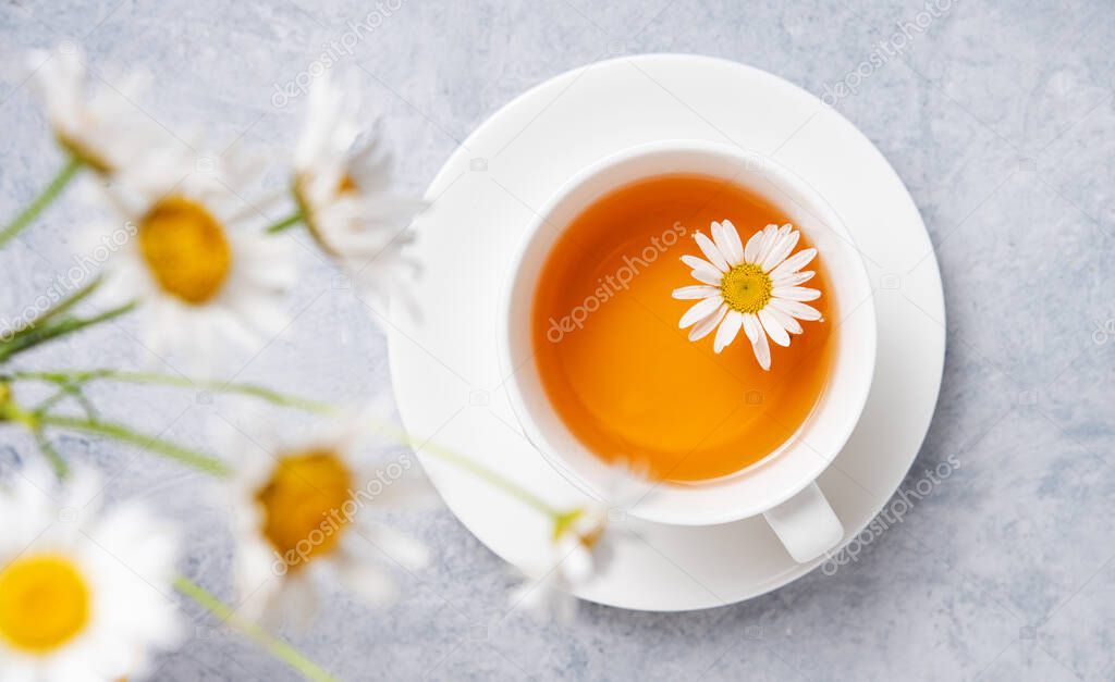 té de manzanilla en una taza blanca con flores margarita sobre un fondo