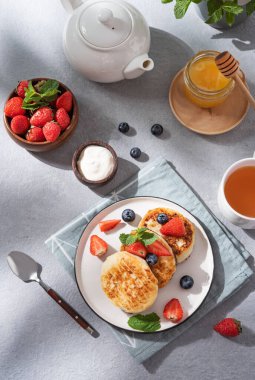 Süzme peynirli krep ya da taze blerryli şurup, bal ve ekşi krema mavi arka planda bir fincan çay ve çaydanlık. Güneşli sabahın erken saatlerinde sağlıklı ve lezzetli bir kahvaltı konsepti. En üst görüntü.