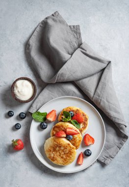 Kahvaltı şurubu için geleneksel Rus yemeği. Ekşi kremalı süzme peynir krepleri ve mavi arka planda peçeteli taze böğürtlenler. Üst görüntü. Dikey yönelim.