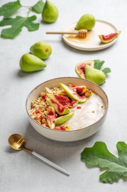 Mısır gevrekli yoğurt, incir ve bal kaşık, meyve ve yapraklı hafif bir arka planda. Kafe menüsü reklamları için sağlıklı ve besleyici kahvaltı konsepti.