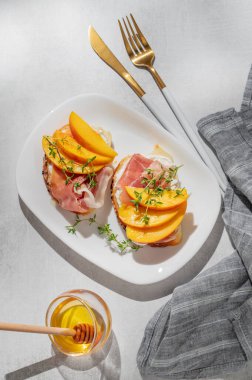 Şeftalili tost, krem peynirli, jambonlu ve ballı kekik, çatal bıçak ve gölgeli bir tabakta. Reklam menüsü ya da kafe afişi için sağlıklı beslenme atıştırmalığı konsepti. Üst görünüm, alanı kopyala.