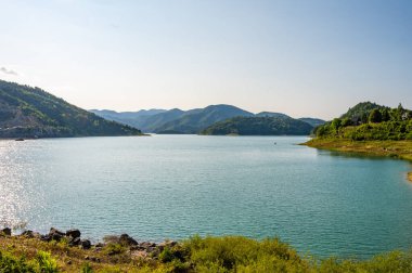 Ormanlık tepelerin arka planında durgun su bulunan bir gölün panoramik ve pitoresk manzarası. Huzurlu doğa ve seyahat kavramı. Tara Ulusal Parkı, Sırbistan.