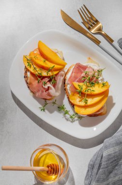 Şeftalili, krem peynirli, jambonlu ve ballı kekik, çatal bıçak ve gölgeli bir tabakta. Reklam menüsü ya da kafe afişi için sağlıklı beslenme atıştırmalığı konsepti. Üst görünüm.