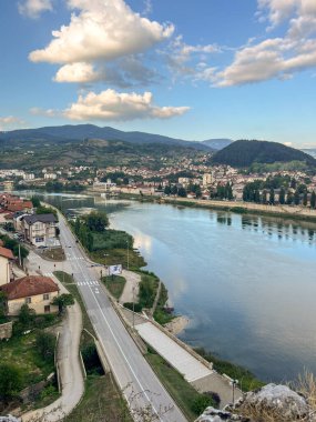 Gün batımında berrak bir gökyüzünün altında ağaçlık tepeler ve dağlarla çevrili sakin bir nehirle çevrili evleri ve binaları olan küçük bir sahil kasabası. Üst Manzara. Visegrad, Bosna-Hersek.