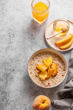 Şeftalili ve fındıklı yulaf ezmesi gri arka planda bal, bir bardak portakal suyu ve taze meyve. Sağlıklı bir vejetaryen yemeği ya da atıştırmalık bir şeyler. Üst görünüm, alanı kopyala.