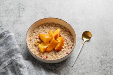 Şeftalili ve fındıklı yulaf ezmesi gri arka planda bal, kaşık ve peçeteli bir kasede. Sağlıklı bir vejetaryen yemeği ya da atıştırmalık bir şeyler. Üst görünüm, alanı kopyala.