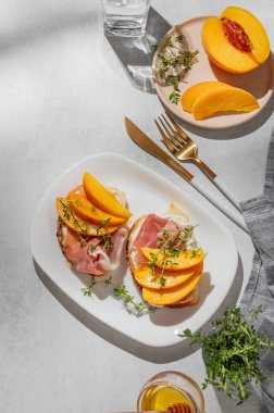 Şeftalili, krem peynirli, jambonlu ve ballı kekik, çatal bıçak ve gölgeli bir tabakta. Reklam menüsü ya da kafe afişi için sağlıklı beslenme atıştırmalığı konsepti. Üst görünüm, alanı kopyala.