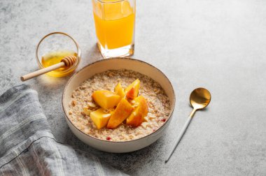 Şeftalili ve fındıklı yulaf ezmesi gri arka planda bal, bir bardak portakal suyu, kaşık ve peçete. Sağlıklı bir vejetaryen yemeği ya da atıştırmalık bir şeyler. Üst görünüm, alanı kopyala.