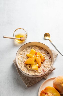 Şeftalili ve fındıklı yulaf ezmesi bal, kaşık ve taze meyveli hafif bir arka planda. Sağlıklı bir vejetaryen yemeği ya da atıştırmalık bir şeyler. Üst görünüm, alanı kopyala.