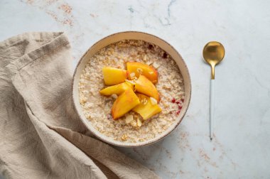 Şeftalili ve fındıklı yulaf ezmesi mermer bir arka planda bal, kaşık ve peçeteyle. Sağlıklı bir vejetaryen yemeği ya da atıştırmalık bir şeyler. Üst görünüm, alanı kopyala.