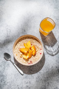 Şeftalili ve fındıklı yulaf ezmesi gri arka planda bal, bir bardak portakal suyu ve sabah gölgesi. Sağlıklı bir vejetaryen yemeği ya da atıştırmalık bir şeyler. Üst görünüm, alanı kopyala.