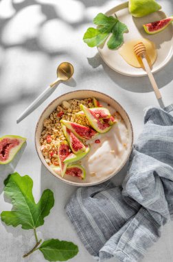 Mısır gevreği ya da müsli ile doğal yoğurt, arka planda hafif bir kase üzerinde incir ve bal, bir kaşık, meyve ve sabah gölgesi. Kahvaltıda sağlıklı ve besleyici detoks yemeği kavramı. Üst görünüm, alanı kopyala.