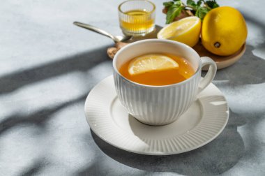 Limonlu, zencefilli, ballı sıcak çay ve turunçgiller ve sabah gölgeleriyle mavi arka planda bir fincanda nane. Soğuk mevsimde dokunulmazlık ve sağlığı desteklemek için bir içki konsepti. Ön görünüm, boşluğu kopyala.