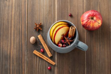 Baharatlı, portakallı, elma dilimli ve ahşap arka planda tarçın çubuklu bir bardak kırmızı şarap. Geleneksel bir sonbahar ya da Noel içkisi konsepti. Üst görünüm, alanı kopyala.