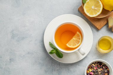 Limonlu sıcak çay, zencefil, bal ve narenciye arkaplanda hafif bir fincanda nane. Soğuk mevsimde dokunulmazlık ve sağlığı desteklemek için bir içki konsepti. Üst görünüm, alanı kopyala.