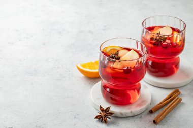 Tarçınlı ve narenciyeli hafif arka planda iki bardak yaban mersini içeceği. Reklam menüsü ya da afiş kafe için geleneksel bir Noel kokteyli ya da portakal, elma ve baharatlı sıcak şarap. Ön görünüm, boşluğu kopyala.