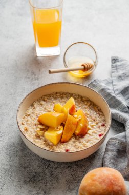 Şeftalili ve fındıklı yulaf ezmesi gri arka planda bal, bir bardak portakal suyu ve peçeteyle. Sağlıklı bir vejetaryen yemeği ya da atıştırmalık bir şeyler. Üst görünüm, alanı kopyala.