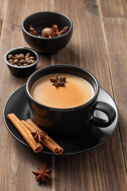 Geleneksel Hint masala çayı sütlü ve baharatlı koyu ahşap arka planda siyah bir fincanda tarçınlı, anason. Menü ya da etnik kafe ya da restoran afişi için sıcak bir içecek konsepti. Ön görünüm, boşluğu kopyala.