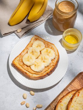 Fıstık ezmeli tost, hafif arka planda muzlu ekmek, serpiştirilmiş fındık, meyve ve sabah gölgesi. Amerikan kahvaltısı için tatlı diyet ve sağlıklı atıştırmalıklar kavramı. Üst görünüm.