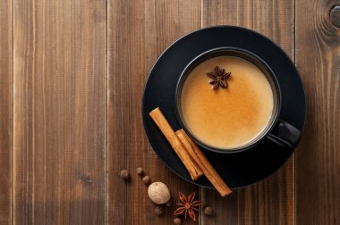 Geleneksel Hint masala çayı sütlü ve baharatlı koyu ahşap arka planda tarçınlı siyah bir fincanda, anason yakın plan. Menü ya da etnik kafe ya da restoran afişi için sıcak bir içecek konsepti. Üst görünüm, alanı kopyala.