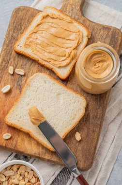 Fıstık ezmeli tost, arka planda tahta bir tahta üzerinde dağınık fındık ve bıçakla. Tatlı vejetaryen diyeti ve Amerikan kahvaltısı için sağlıklı atıştırmalıklar. Üst görünüm.