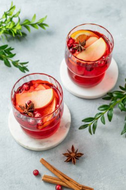 Tarçınlı ve yeşil dallı hafif arka planda iki bardakta bir kızılcık içeceği. Reklam menüsü ya da afiş kafe için geleneksel bir Noel kokteyli ya da portakal, elma ve baharatlı sıcak şarap. Üst görünüm, alanı kopyala.