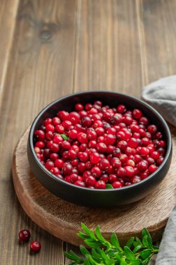 Koyu bir kasede, yeşil dallı ve peçeteli taze kızılcıklar. Kırsal tarzda sağlıklı yaban mersini kavramı. Boşluğu kopyala.