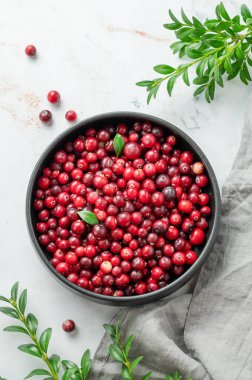 Açık mermer arka planda koyu bir kasede yeşil dallı ve peçeteli taze kızılcıklar. Sağlıklı yabani böğürtlen kavramı. Üst görünüm, alanı kopyala.