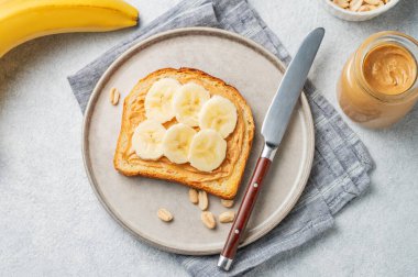 Fıstık ezmeli tost ve muz hafif arka planda fındık ve bıçaklı bir tabakta. Amerikan kahvaltısı için besleyici ve sağlıklı atıştırmalıklar. Üst görünüm, alanı kopyala.