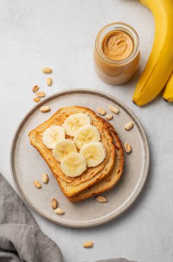 Fıstık ezmeli tost ve muz hafif arka planda, fındıklı, serpilmiş kavanoz ve peçeteli. Amerikan kahvaltısı için besleyici ve sağlıklı atıştırmalıklar. Üst görünüm, alanı kopyala.