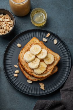 Fıstık ezmeli tost ve muz siyah bir tabakta fındık ve bal ile birlikte. Amerikan kahvaltısı için besleyici ve sağlıklı atıştırmalıklar. Üst görünüm.