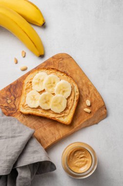 Fıstık ezmeli tost ve muz, arka planda hafif bir tahta üzerinde fındık kavanozu ve peçeteyle birlikte. Amerikan kahvaltısı için besleyici ve sağlıklı atıştırmalıklar. Üst görünüm, alanı kopyala.