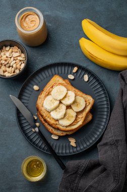 Fıstık ezmeli tost ve muz siyah bir tabakta fındık, bal ve meyveli. Amerikan kahvaltısı için besleyici ve sağlıklı atıştırmalıklar. Üst görünüm.