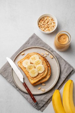Fıstık ezmeli tost ve muz hafif arka planda, fındık kavanozu, yayılma ve bıçakla birlikte bir tabakta. Amerikan kahvaltısı için besleyici ve sağlıklı atıştırmalıklar. Üst görünüm, alanı kopyala.