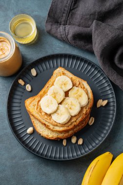 Fıstık ezmeli tost ve muz siyah bir tabakta fındık, bal ve meyveli. Amerikan kahvaltısı için besleyici ve sağlıklı atıştırmalıklar. Üst görünüm.