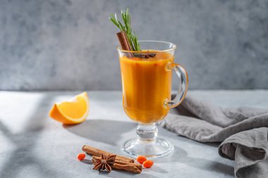 Mavi arka planda, portakal, baharat ve gölgeli mavi bir bardakta deniz dikenli bitkisel çay. Bağışıklığı arttırmak için sıcak sonbahar organik içeceği konsepti. Ön görünüm, boşluğu kopyala.