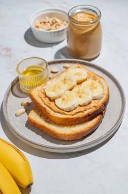 Fıstık ezmeli tost ve muz mermer arka planda meyve, fındık, bal ve sabah gölgesi olan bir tabakta. Amerikan kahvaltısı için tatlı diyet ve sağlıklı atıştırmalıklar kavramı.