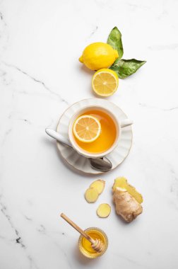 Ballı, narenciyeli ve köklü beyaz mermer arka planda taze limon ve zencefilli bir fincan sıcak çay. Dokunulmazlığı ve sağlığı arttırmak için doğal içecek kavramı. Üst görünüm, alanı kopyala.