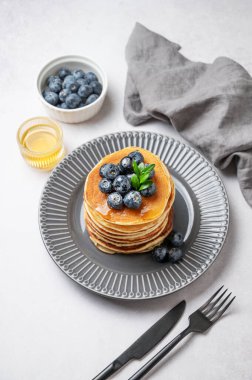 Bal, böğürtlen, peçete ve çatal bıçaklı gri bir tabakta taze yaban mersinli krep yığını. Lezzetli ve besleyici bir kahvaltı ya da brunch konsepti. Üst görünüm, alanı kopyala.