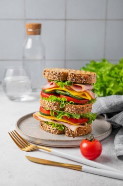 Jambonlu, peynirli, marullu ve sebzeli üçlü sandviç tabakta tam tahıllı ekmek ve arka planda bir bardak su. Kavram, taze ve sağlıklı bir atıştırmalıktır. Ön görünüm