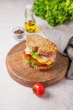 Jambonlu, peynirli, marullu ve sebzeli sandviç beton bir arka planda, ahşap bir tahtada, baharatlı, taze salatalı ve peçeteli. Sağlıklı, ev yapımı atıştırmalıklar. Üst görünüm, alanı kopyala.